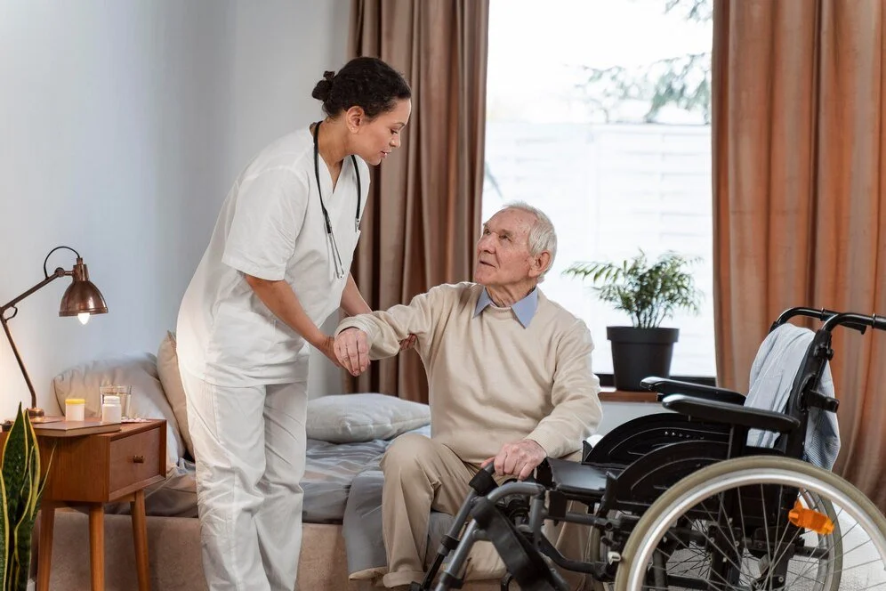 Nurse assisting elderly man in wheelchair inside a bright assisted living room, reflecting personalized in-room medical care and warm support at MorningStar of Pasadena.