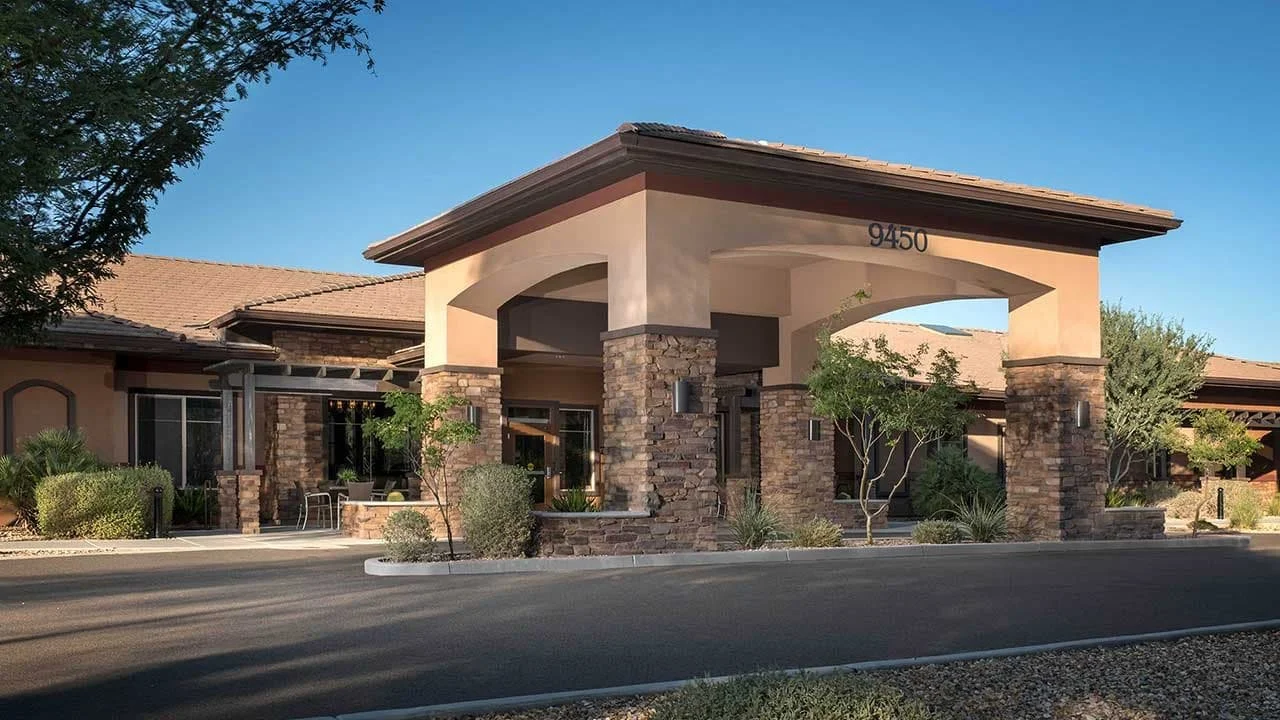 Front entrance of Mosaic Gardens Memory Care at Scottsdale, featuring modern architecture with stone accents and shaded drive-up access for residents and visitors.