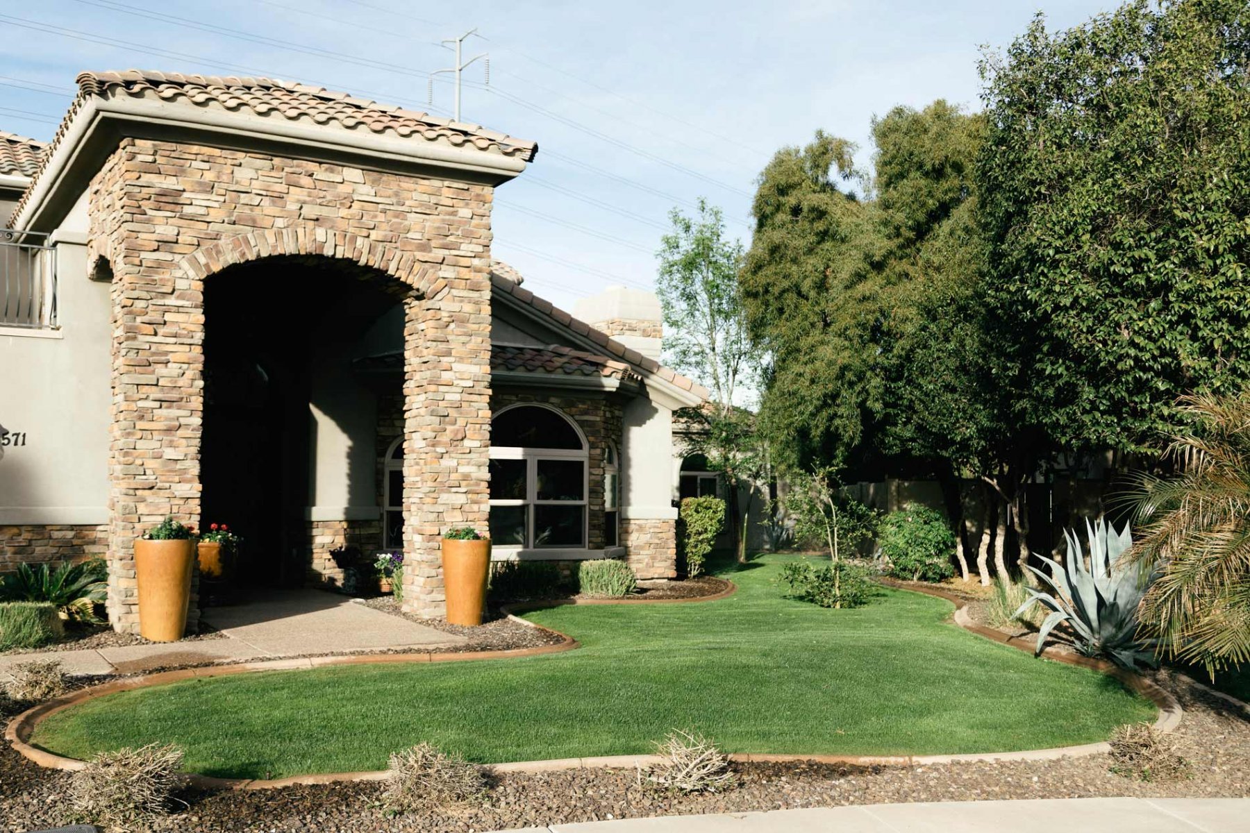 Front view of Central Scottsdale Assisted Living facility featuring a beautifully maintained green lawn, stone facade entrance, and lush trees providing a welcoming and peaceful atmosphere.