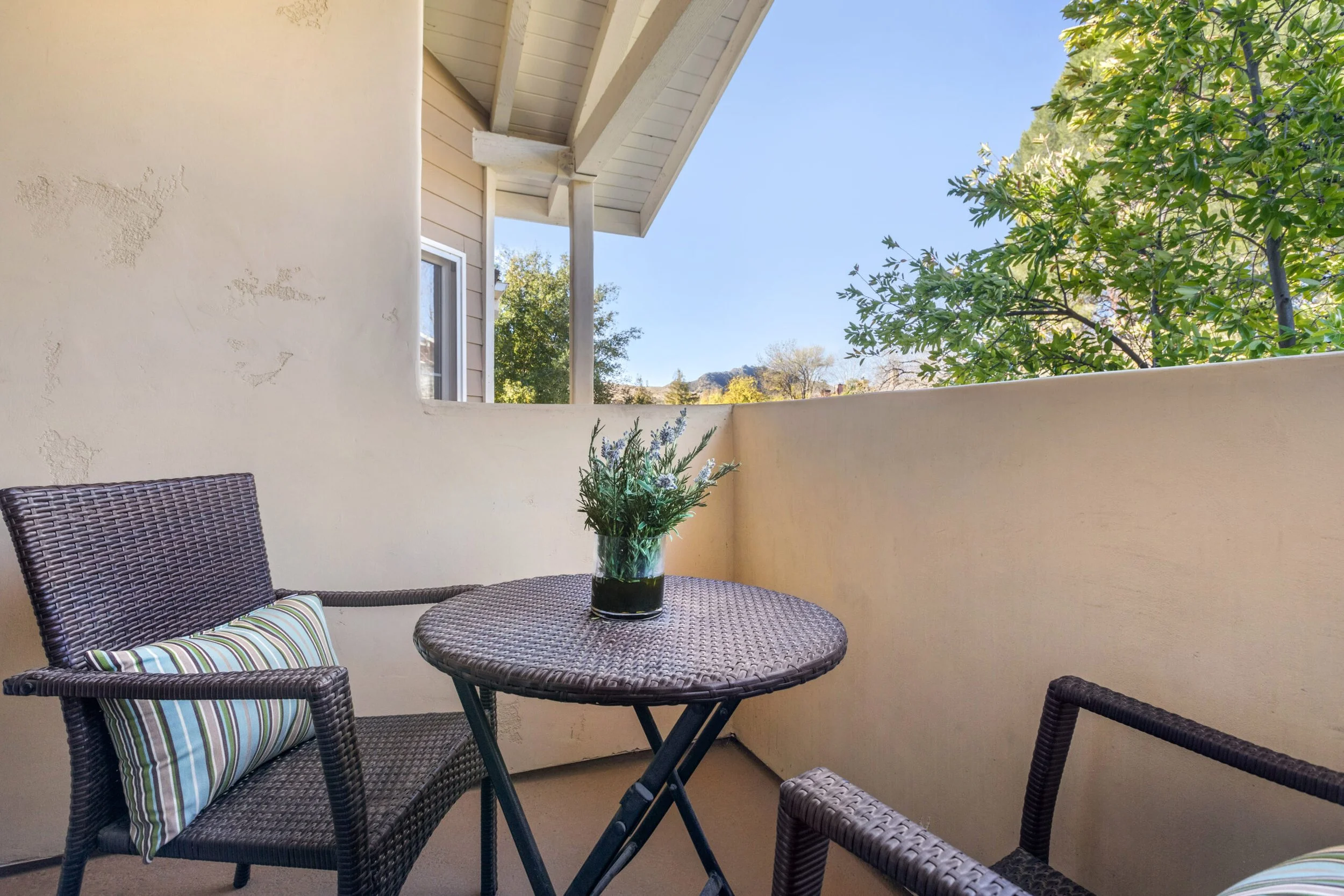 Private balcony at Meadowbrook at Agoura Hills featuring wicker chairs, a round table with potted greenery, and views of surrounding trees—offering residents a peaceful outdoor retreat.
