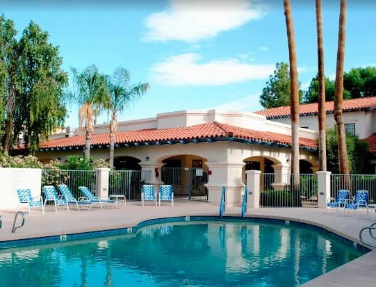Outdoor pool area at Weyrich Health Care Center at Westminster Village, featuring lounge chairs, palm trees, and Spanish-style architecture in a serene Scottsdale setting.