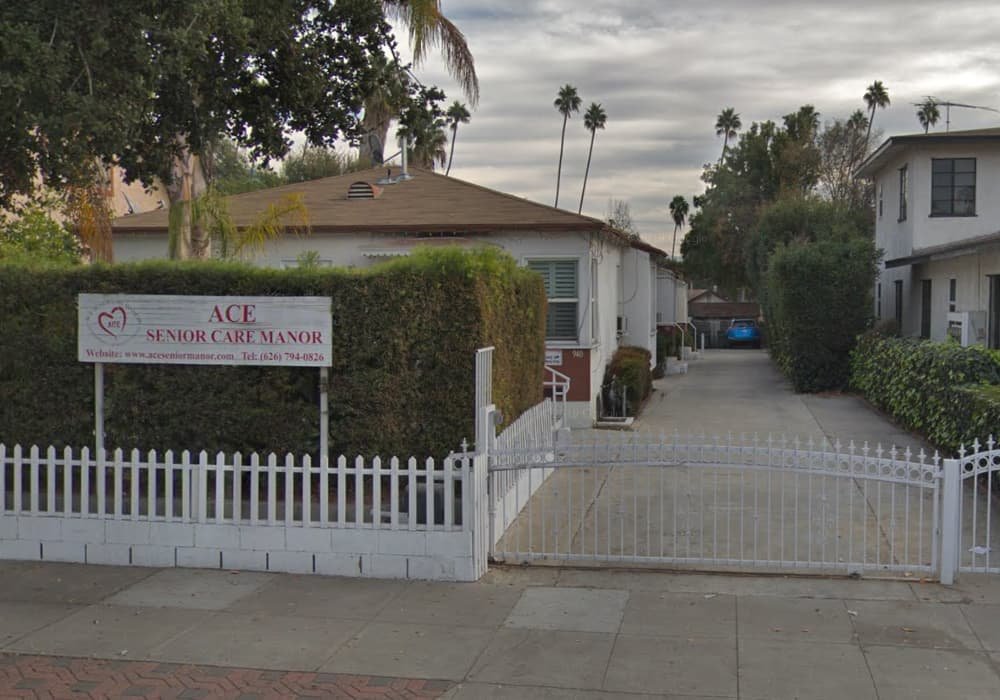 Exterior front view of ACE Senior Care Manor assisted living home in Pasadena, CA, with white fence, driveway, and facility sign by the hedge.