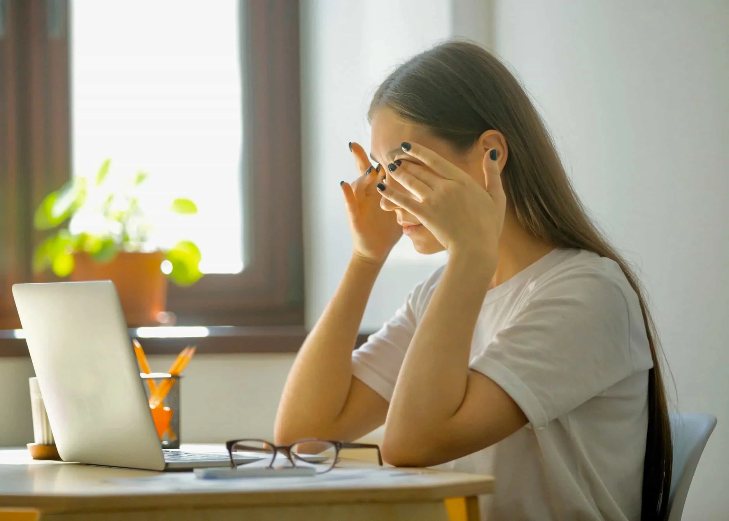 Young woman rubbing her tired eyes while working at a laptop, showing signs of digital eye strain