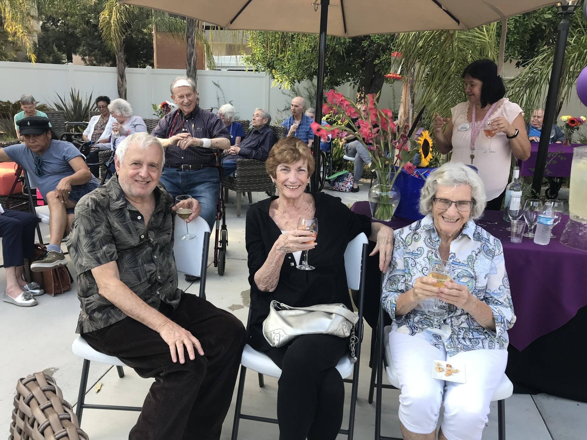 Happy senior residents enjoy time outdoors in the outdoor courtyard, chatting and smiling in a warm, friendly atmosphere.