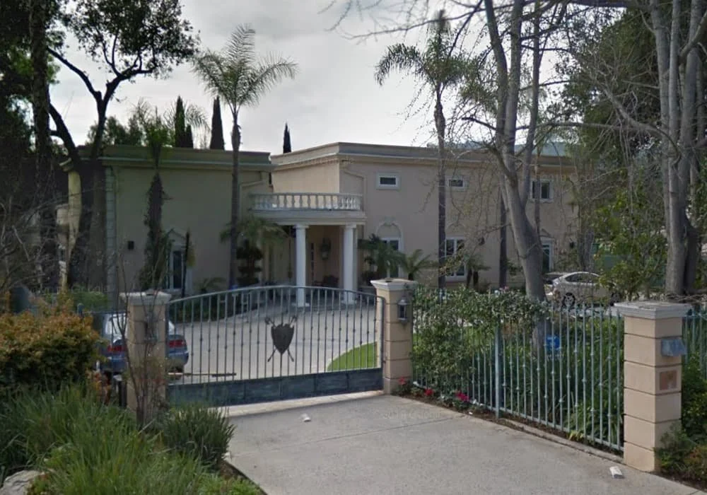 Front view of An Elite Chateau, a Mediterranean-style luxury residence with a gated driveway, palm trees, and a columned entrance.