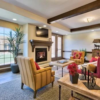 Comfortable resident lounge at Lone Mountain Memory Care featuring warm-toned seating, fireplace, natural lighting, and home-like décor designed to foster relaxation and familiarity.