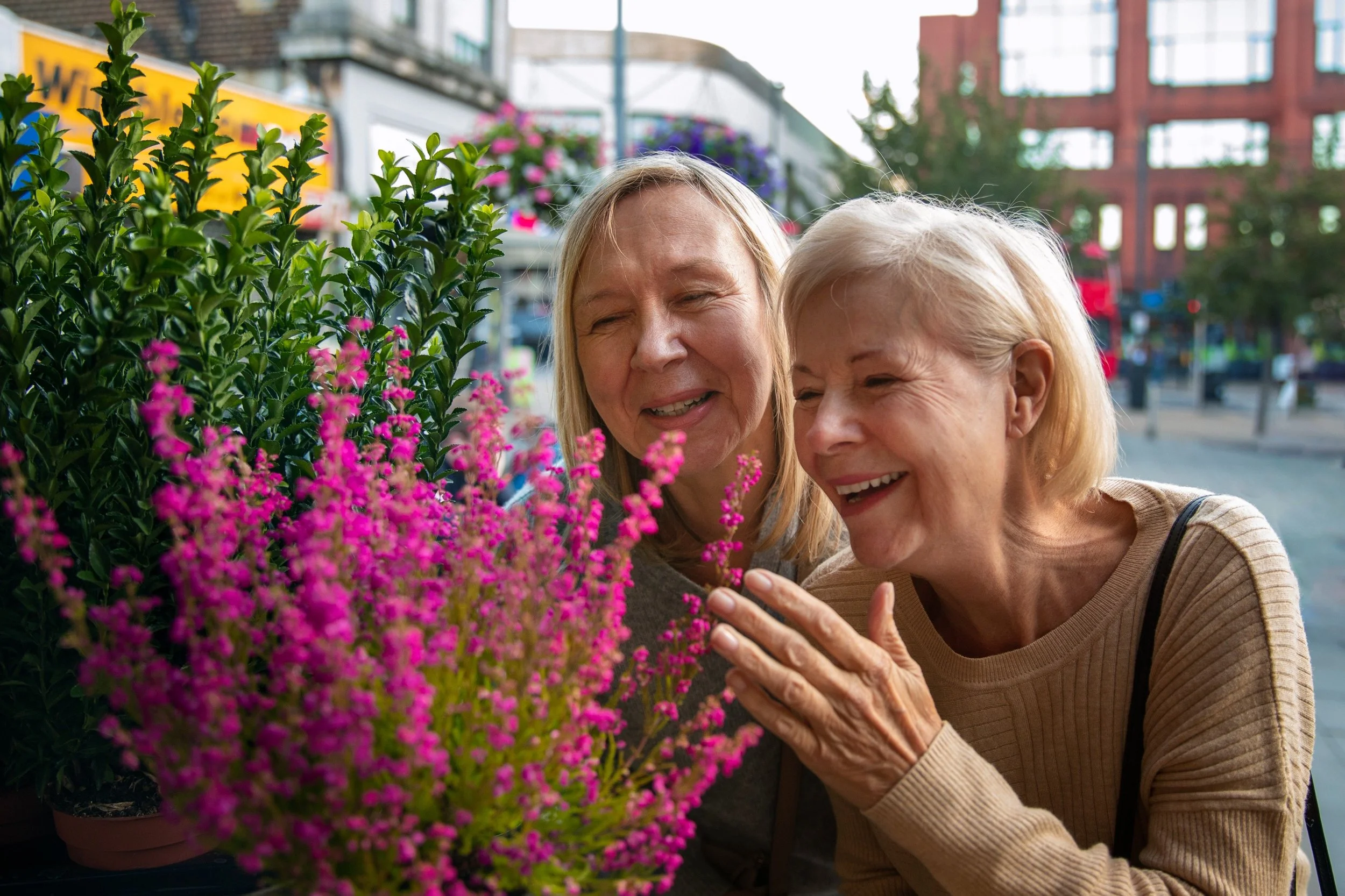 Two smiling senior women enjoying blooming flowers outdoors, representing the joyful, social, and enriching lifestyle offered at Hands of Care assisted living in Scottsdale.