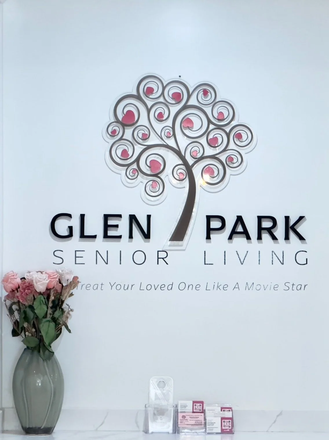 Reception area at Glen Park Senior Living Mariposa Street with logo, flowers, and cabinetry