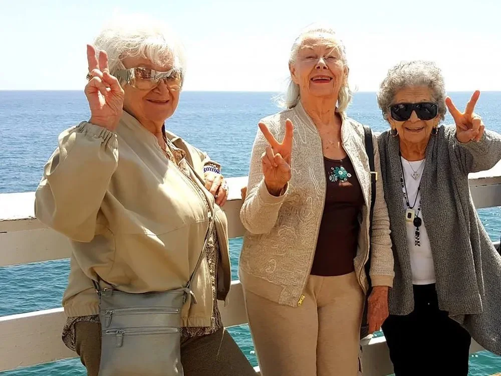 Three senior women smiling and making peace signs while enjoying a sunny day at the beach
