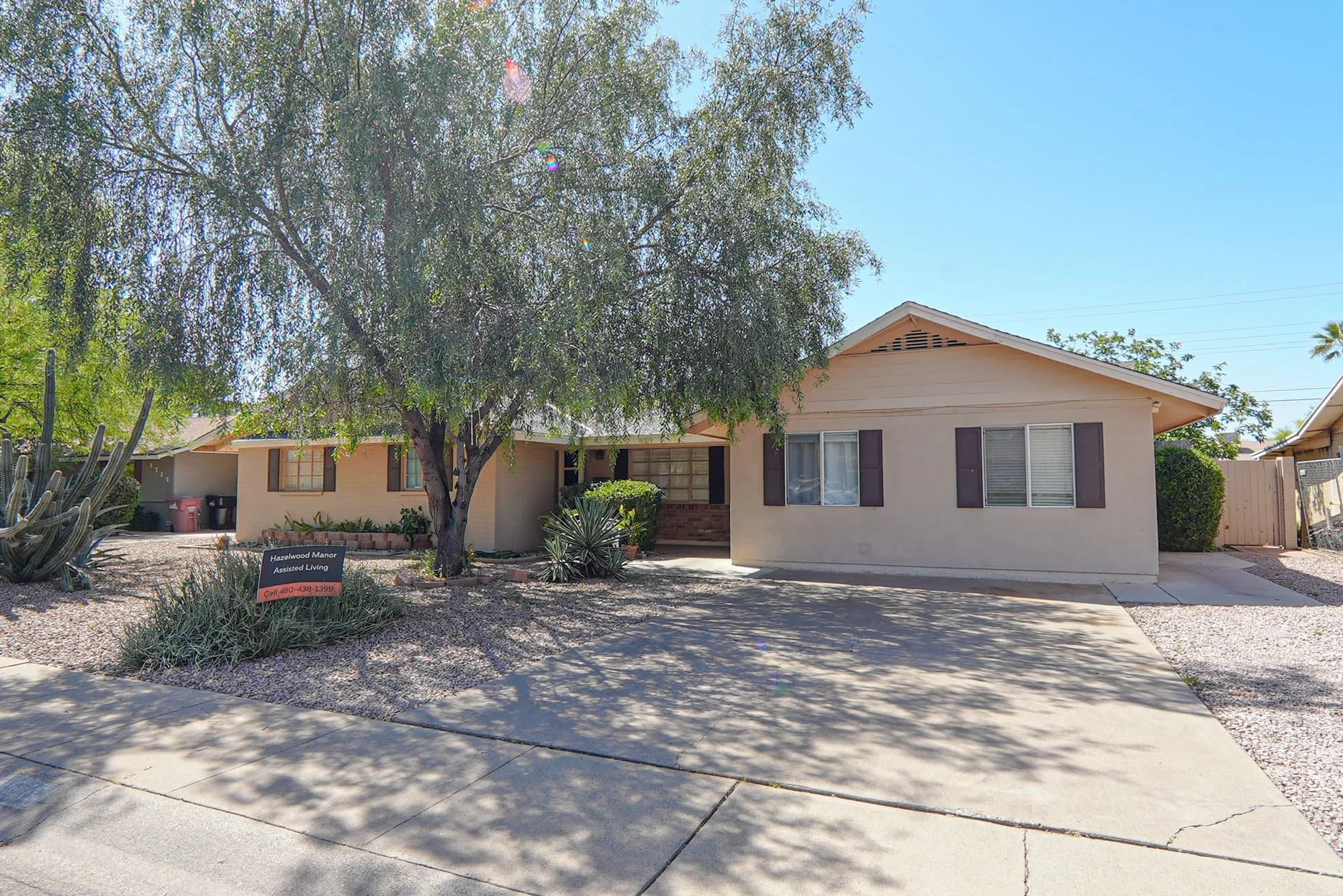 Exterior view of Hazelwood Manor Assisted Living in Scottsdale, AZ, showing the front entrance, natural landscaping, and shaded surroundings.