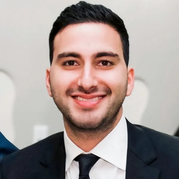 Young male professional in a dark suit and tie smiling at the camera.