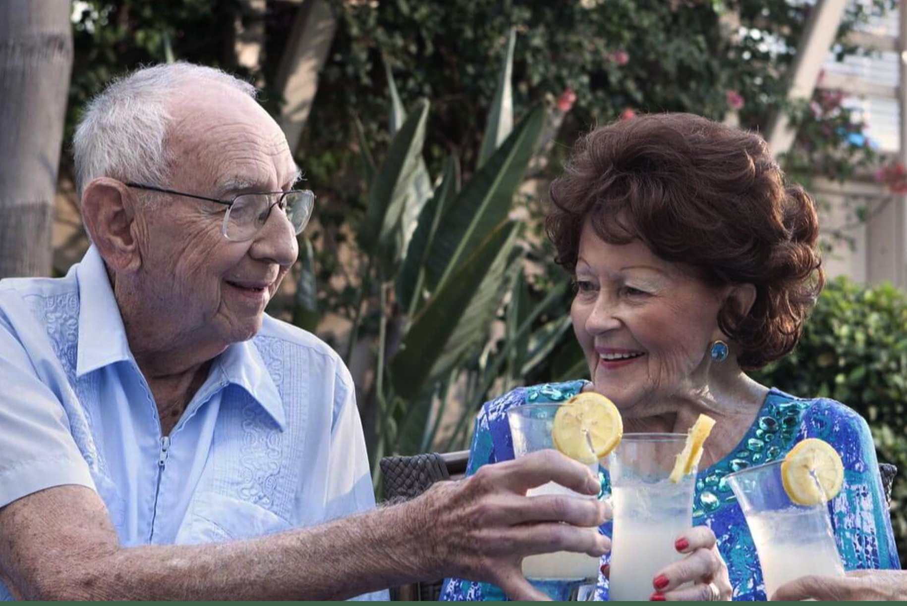 An elderly couple enjoying refreshing lemonade outdoors, smiling at each other in a relaxed and welcoming senior living community setting