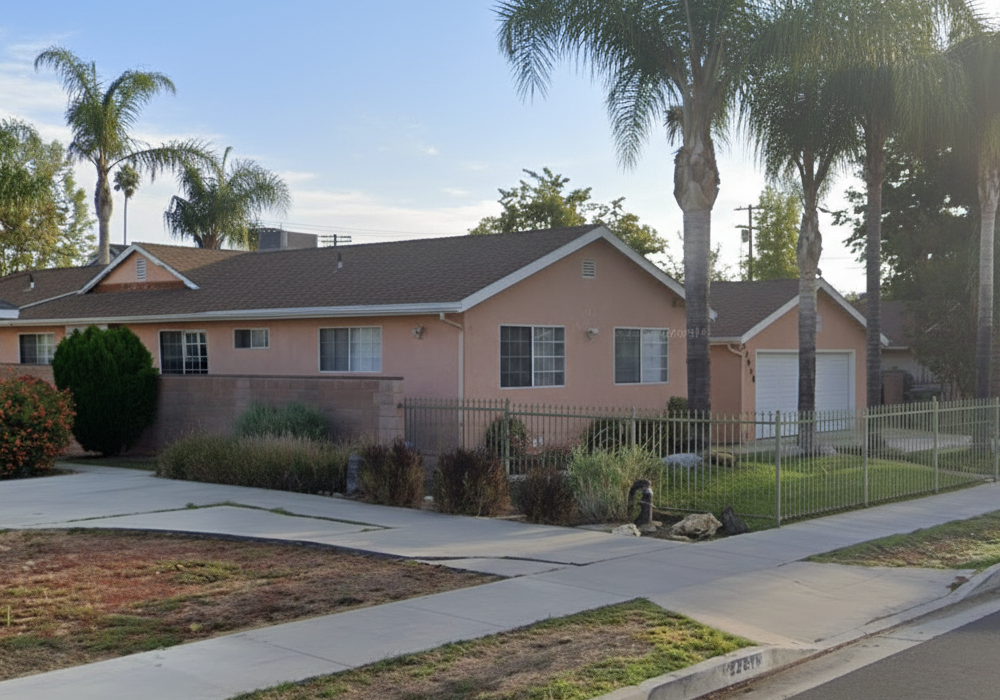 Single-story peach-colored assisted living home with a fenced front yard, tall palm trees, and a clean concrete driveway on Kittridge Street in West Hills, CA.