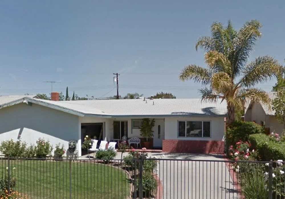 Single-story Woodland West Homes III residential care home with gated driveway, green front lawn, and palm tree in West Hills, California.