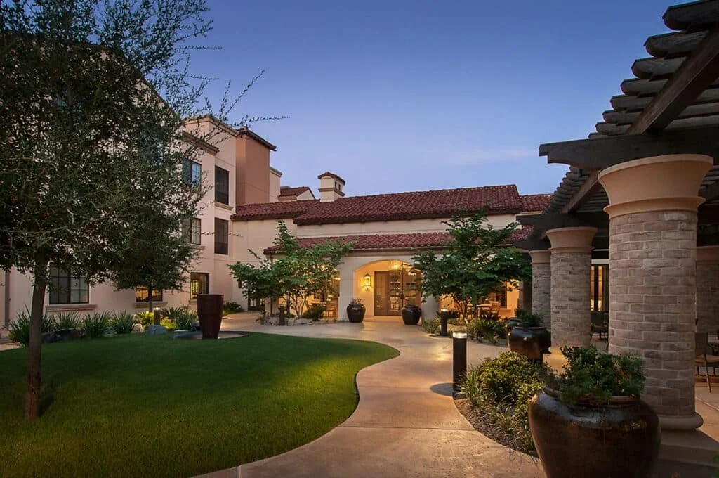 Evening view of the courtyard at Maravilla Scottsdale Assisted Living, featuring Mediterranean architecture, landscaped greenery, and a welcoming outdoor setting