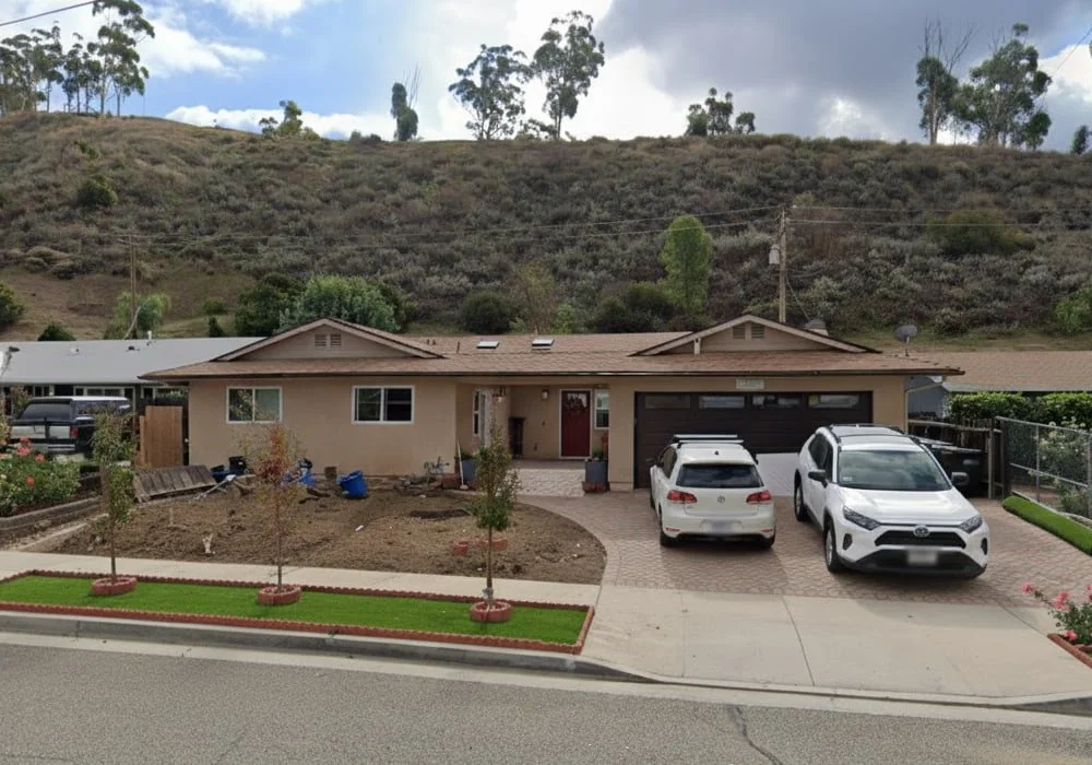 Front view of Alta Vista Simi #2 assisted living home in Simi Valley, showing a single-story beige house with two parked cars and a hillside backdrop.
