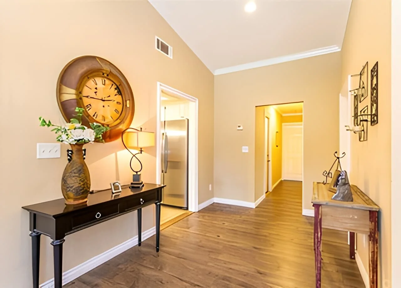 Interior hallway at Agape Senior Living featuring warm-toned walls, hardwood floors, decorative clocks, and soft lighting, creating a welcoming and residential ambiance.