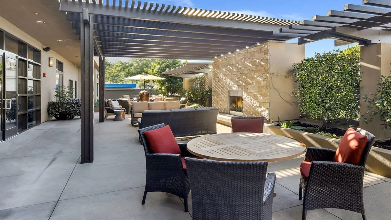 Outdoor patio area at Ivy Park at Burbank featuring shaded seating, cozy fireplace, and lush greenery, offering residents a relaxing and elegant environment for socializing or quiet time.