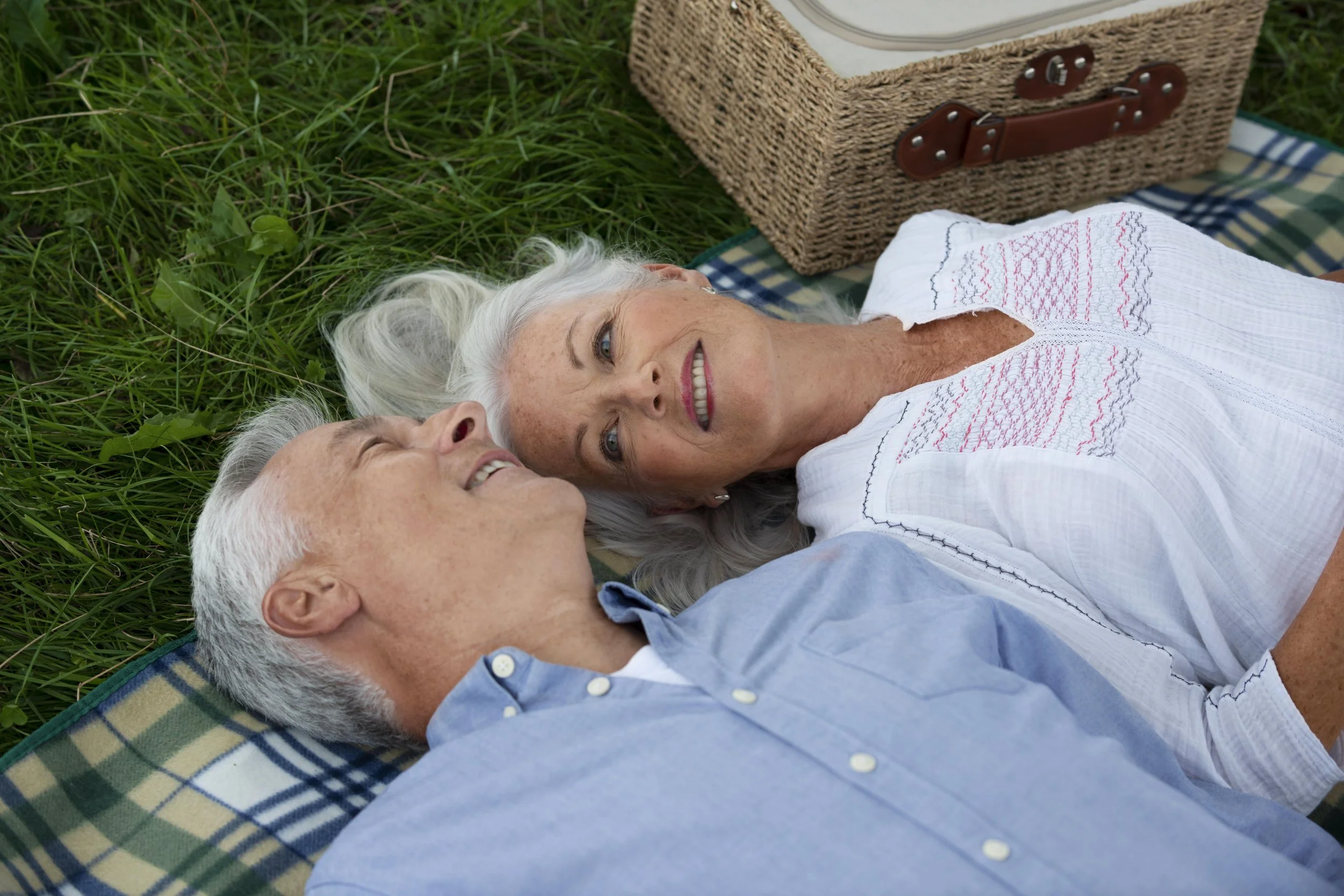 Senior couple relaxing on a picnic blanket in a grassy field, smiling at each other during a peaceful outdoor moment symbolizing the warm, personal atmosphere at Arizona Royal Care Home in Scottsdale