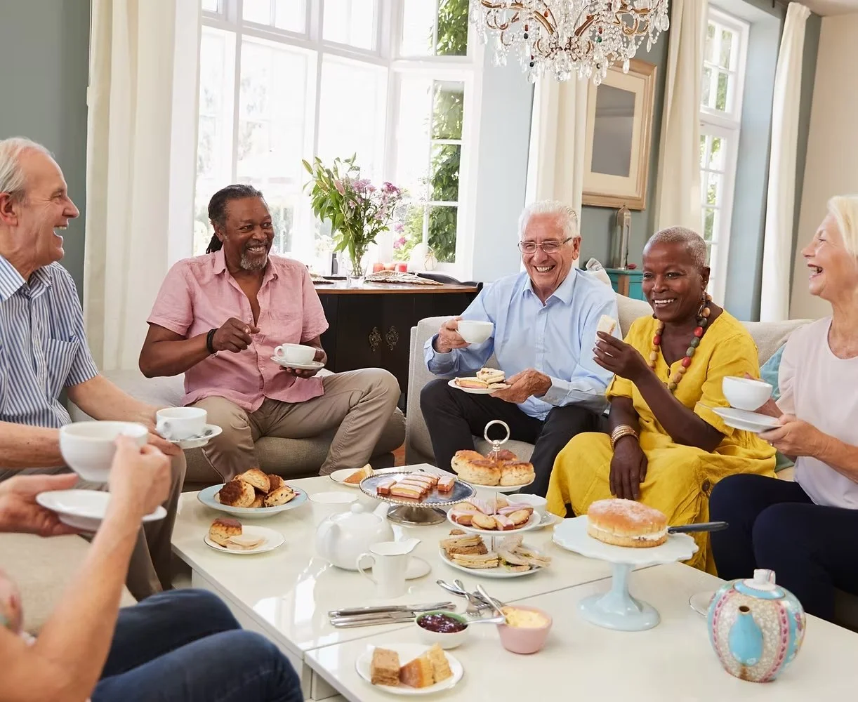 A group of senior residents enjoying tea and pastries together in a bright and elegant living room, fostering social connections and a warm community atmosphere.