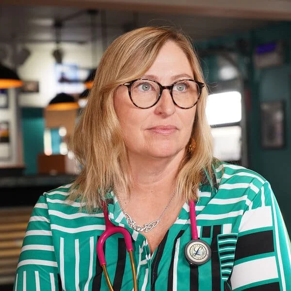 Thoughtful female doctor with round glasses and stethoscope sitting in a clinic.