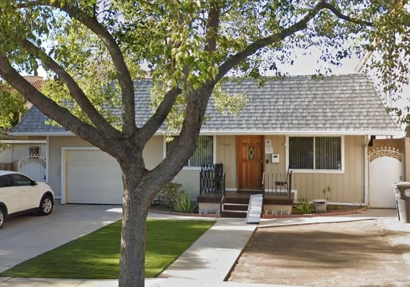 Exterior view of Alameda Board & Care at 1129 Alameda Ave in Glendale, California, showing a single-story home with a front yard tree, driveway, and entry walkway.