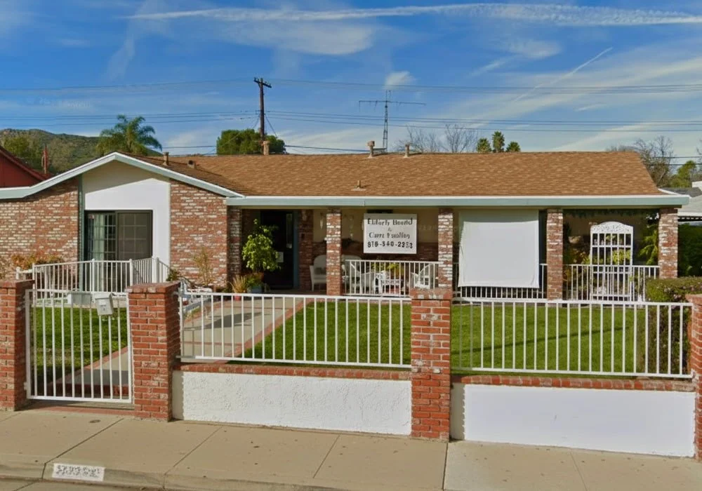 Front exterior view of Kim’s Love & Care assisted living home in West Hills, California, showing a single-story brick house with a white fence and green lawn.