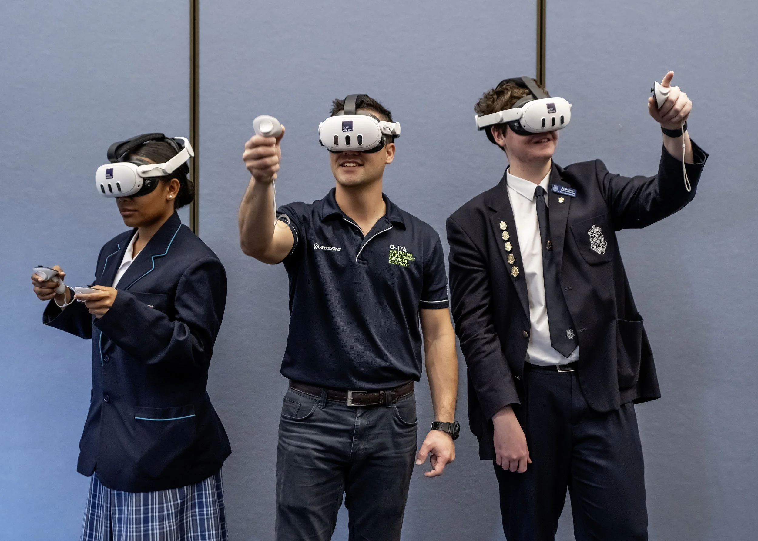 Three people wearing virtual reality headsets, standing in a line, smiling, with one giving a thumbs-up gesture.