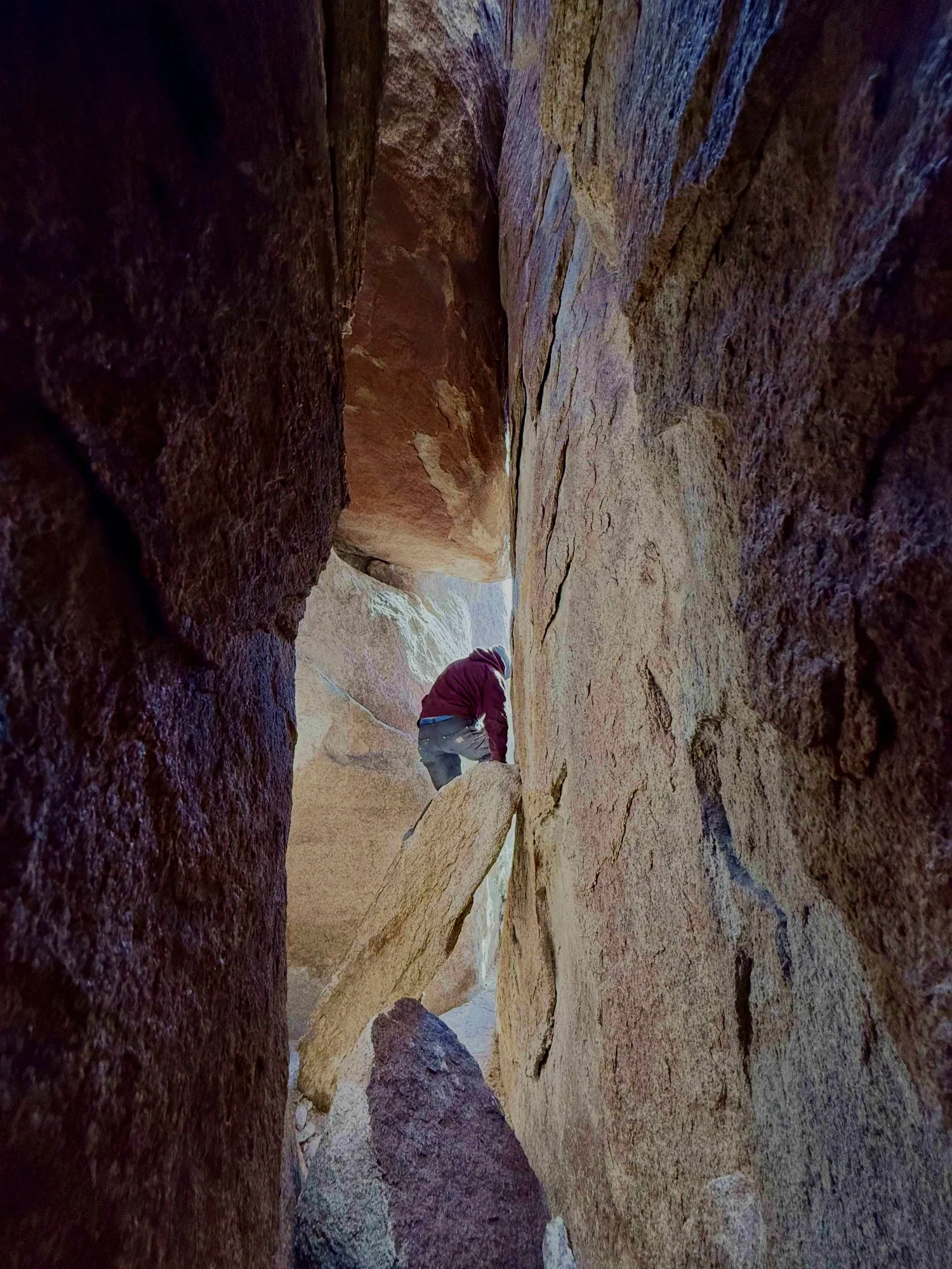 A person climbing a narrow rocky crevice between large granite walls on The Great Misdirect