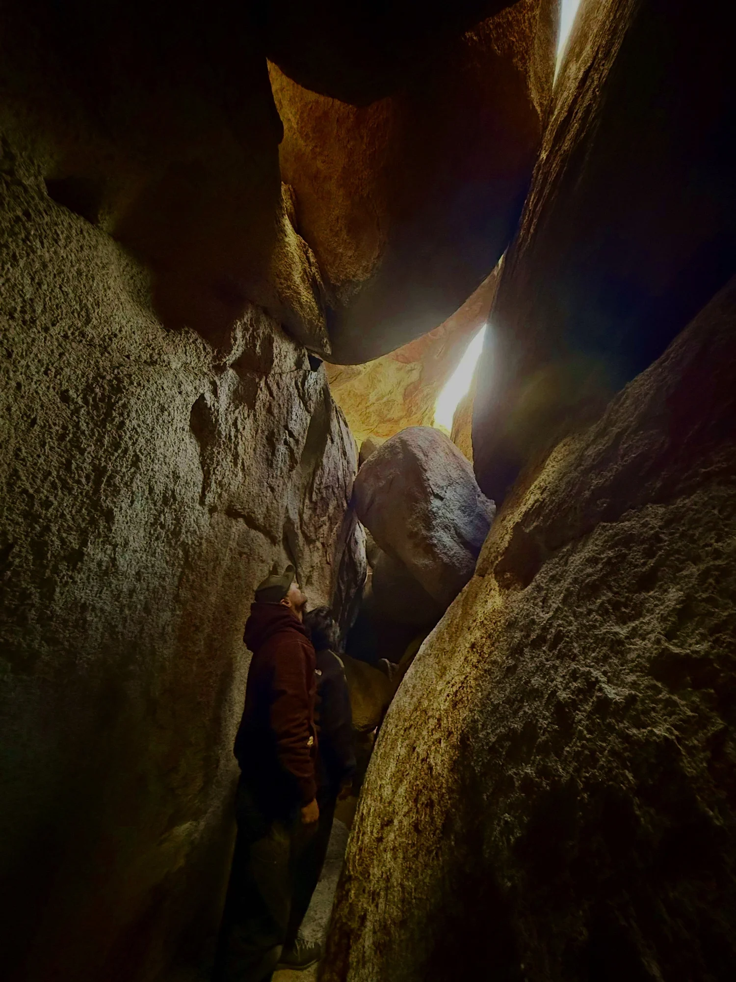 People exploring a narrow rocky cave passage on The Great Misdirect in Joshua Tree National Park