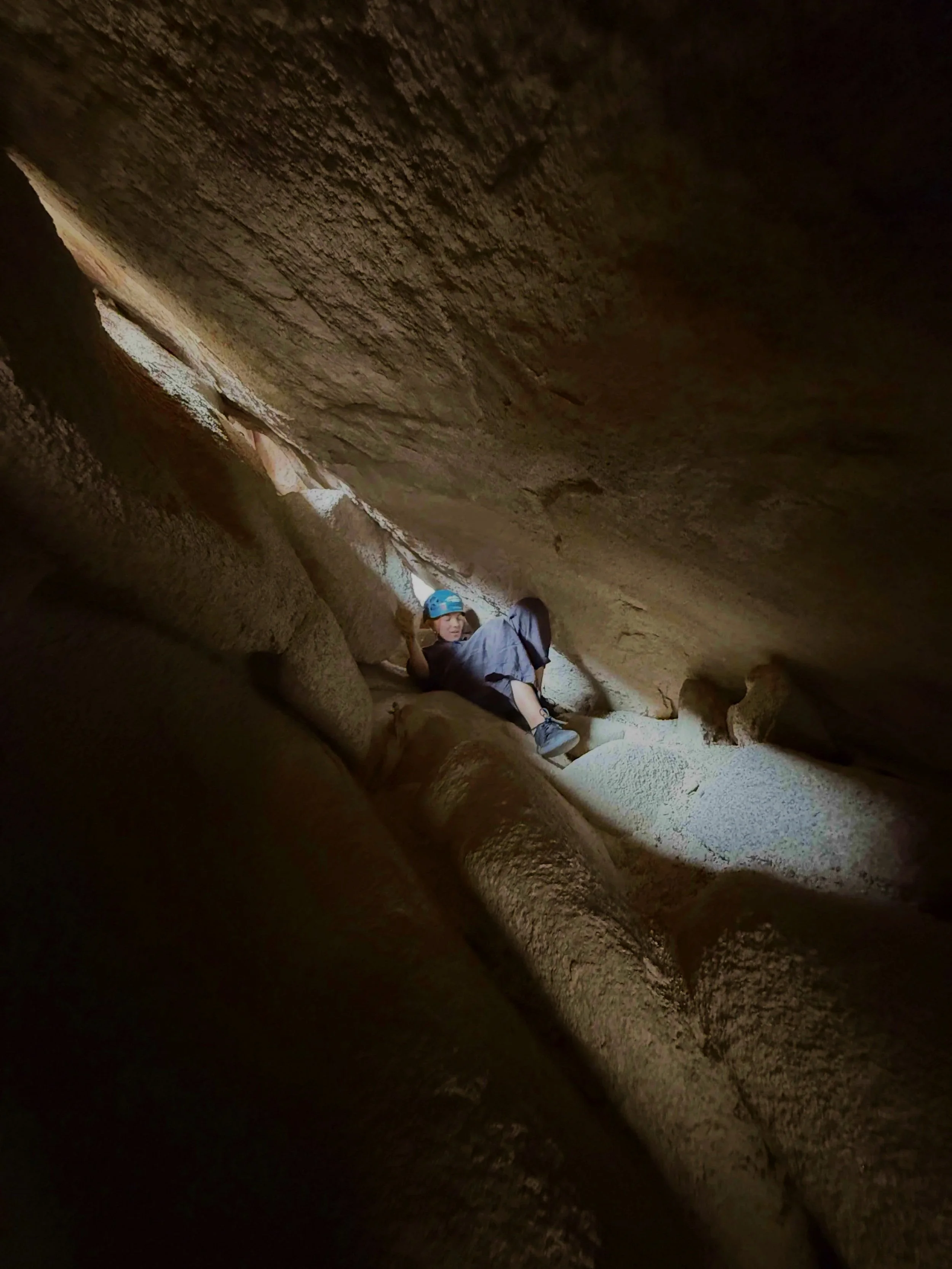 A person wearing a blue helmet inside a narrow cave or crevice with rocky walls.