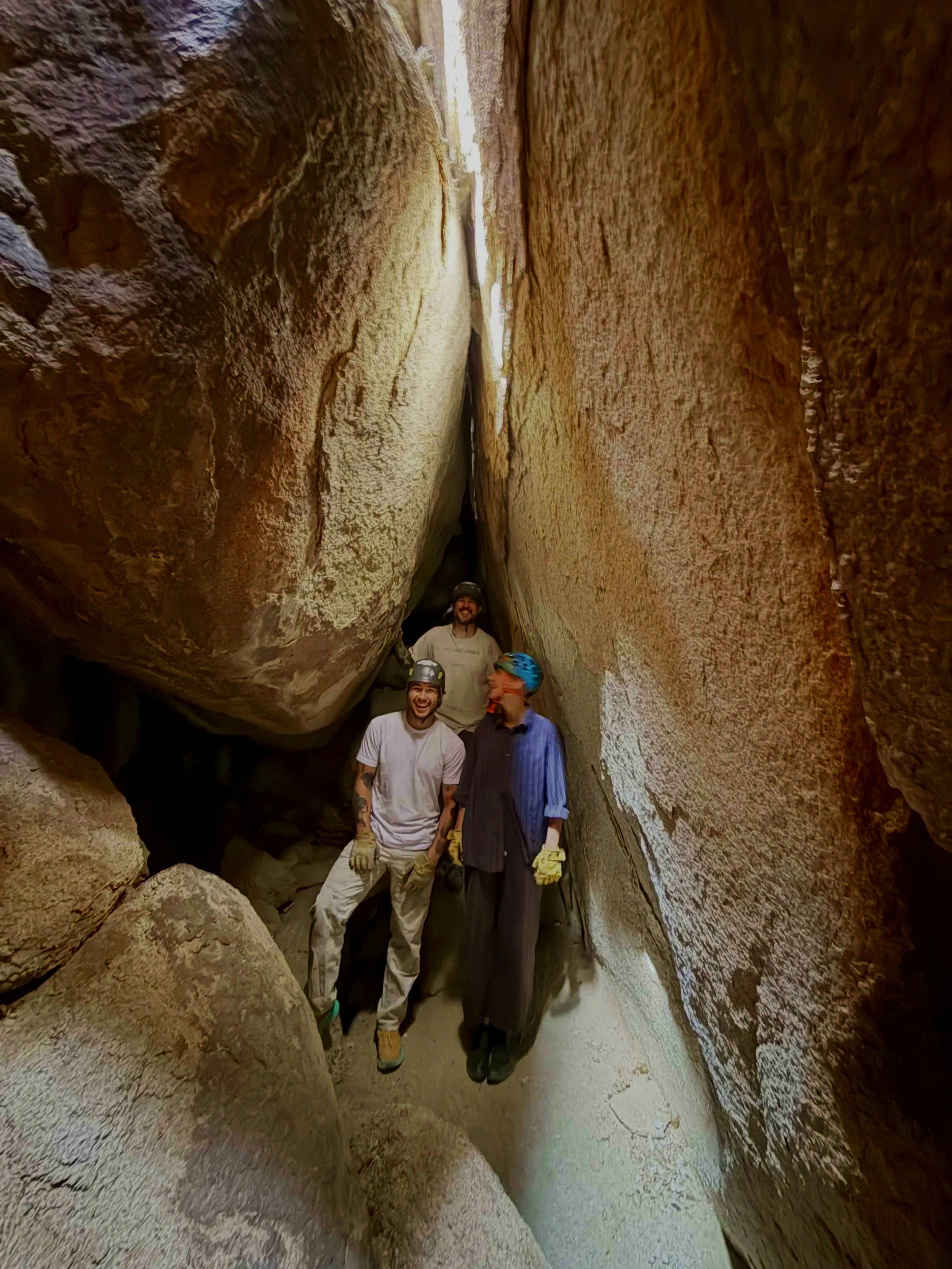 Three people standing inside a narrow, rocky canyon with high walls on either side, smiling and posing for a photo.