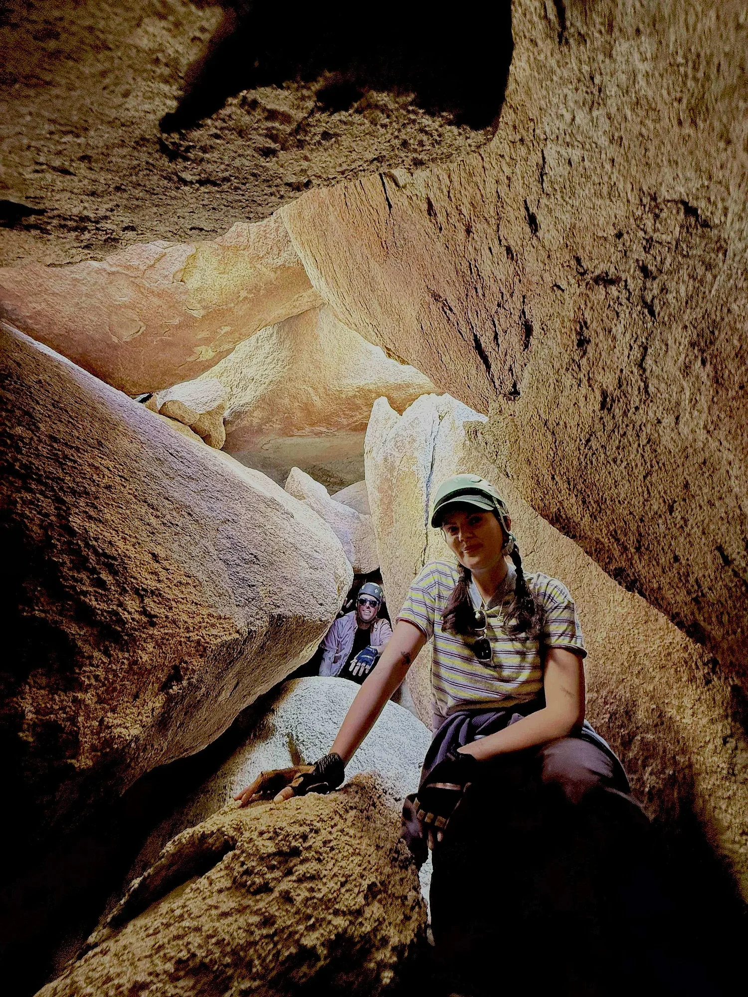 Two women inside a narrow rocky canyon, climbing over large boulders, smiling on a Summit Climbing Guides adventure