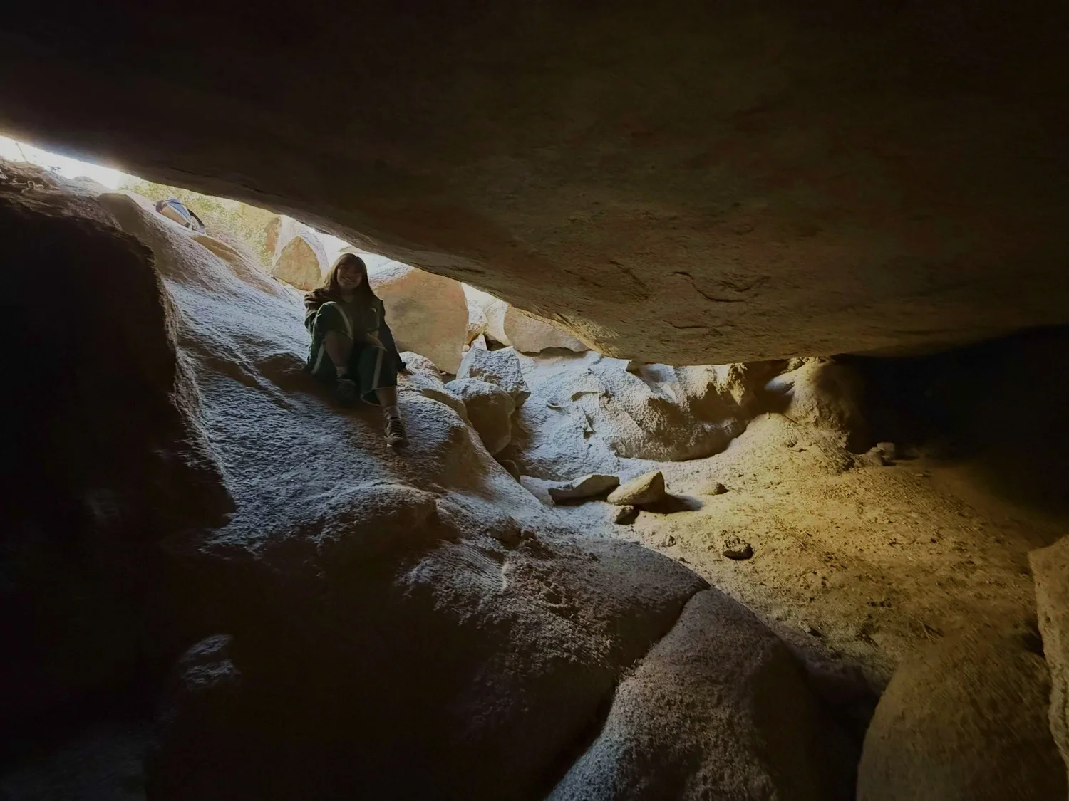 A woman sitting on rocks inside a cave on The Mad Hatter route with sunlight shining in from the opening above