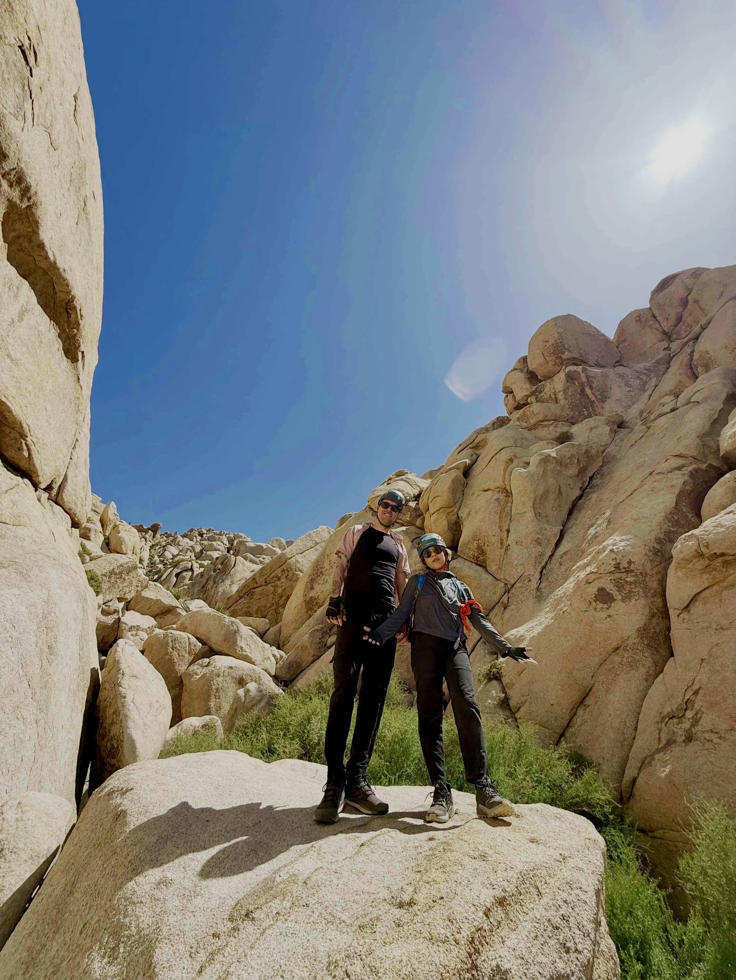 Two people in outdoor gear and helmets standing on a large rock with a sweeping desert canyon view on The Mad Hatter route