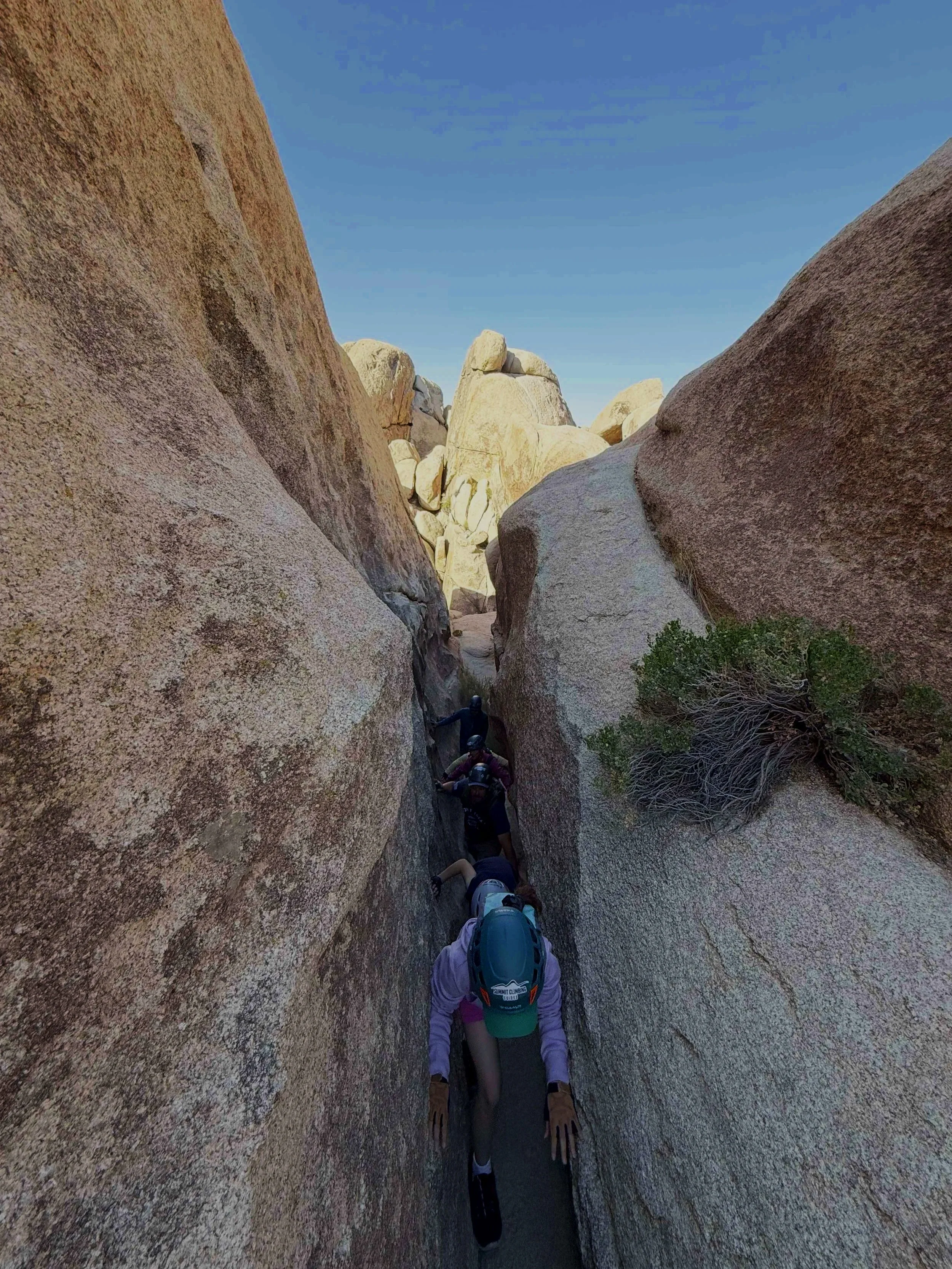 Two adventurers climbing through a narrow slot canyon under clear blue sky