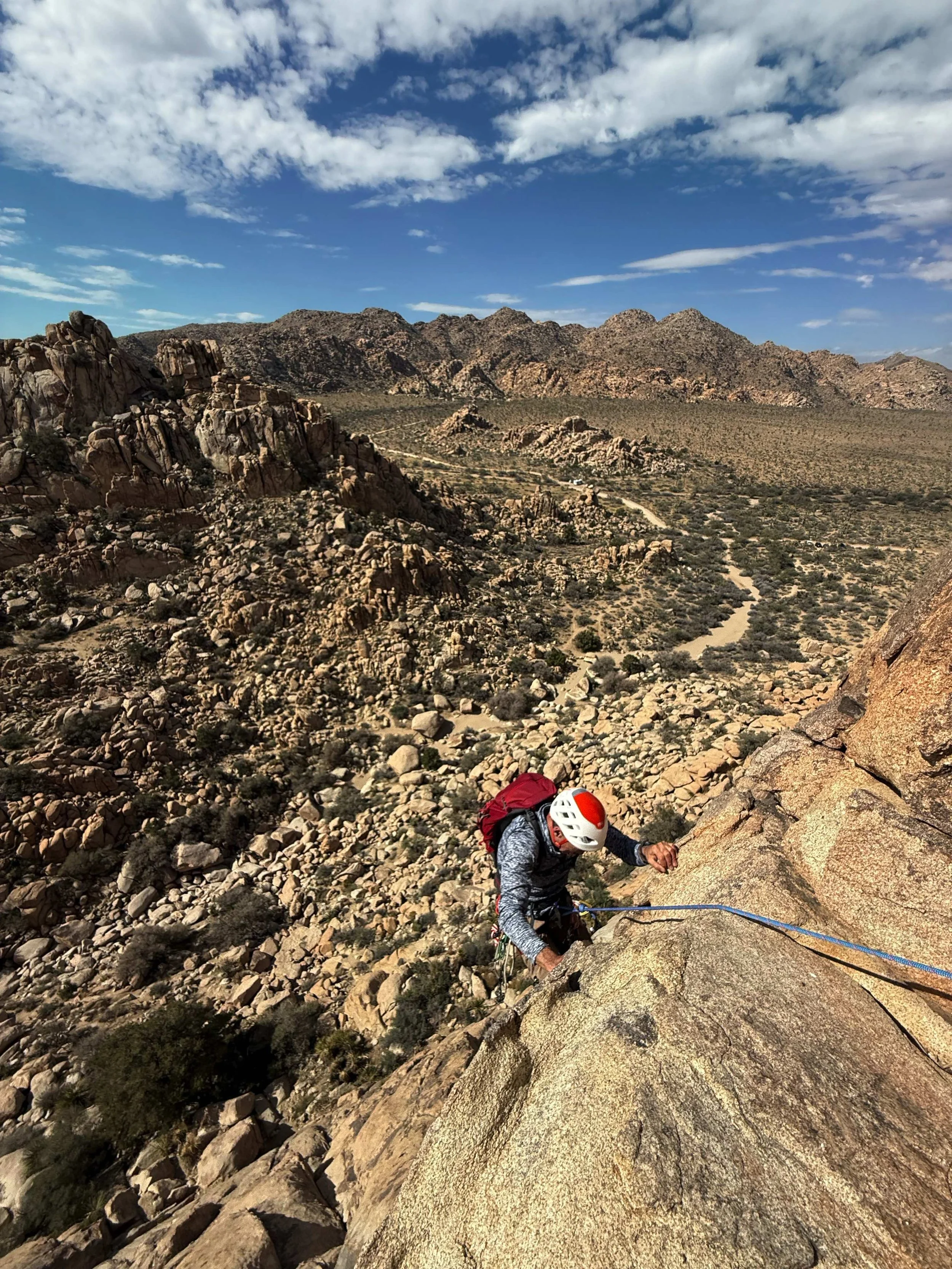 Climber high on a multi-pitch route at Lost Horse Wall with Joshua Tree desert below — Summit Climbing Guides
