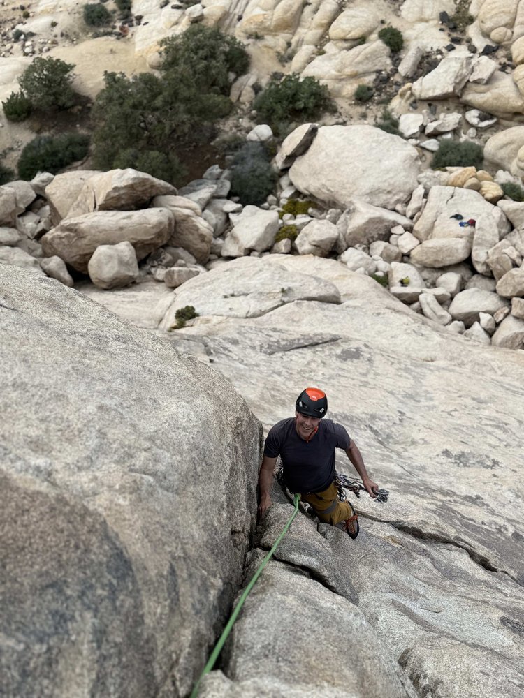 Climber on real Joshua Tree granite with safety harness and climbing gear, smiling during a guided rock climbing session
