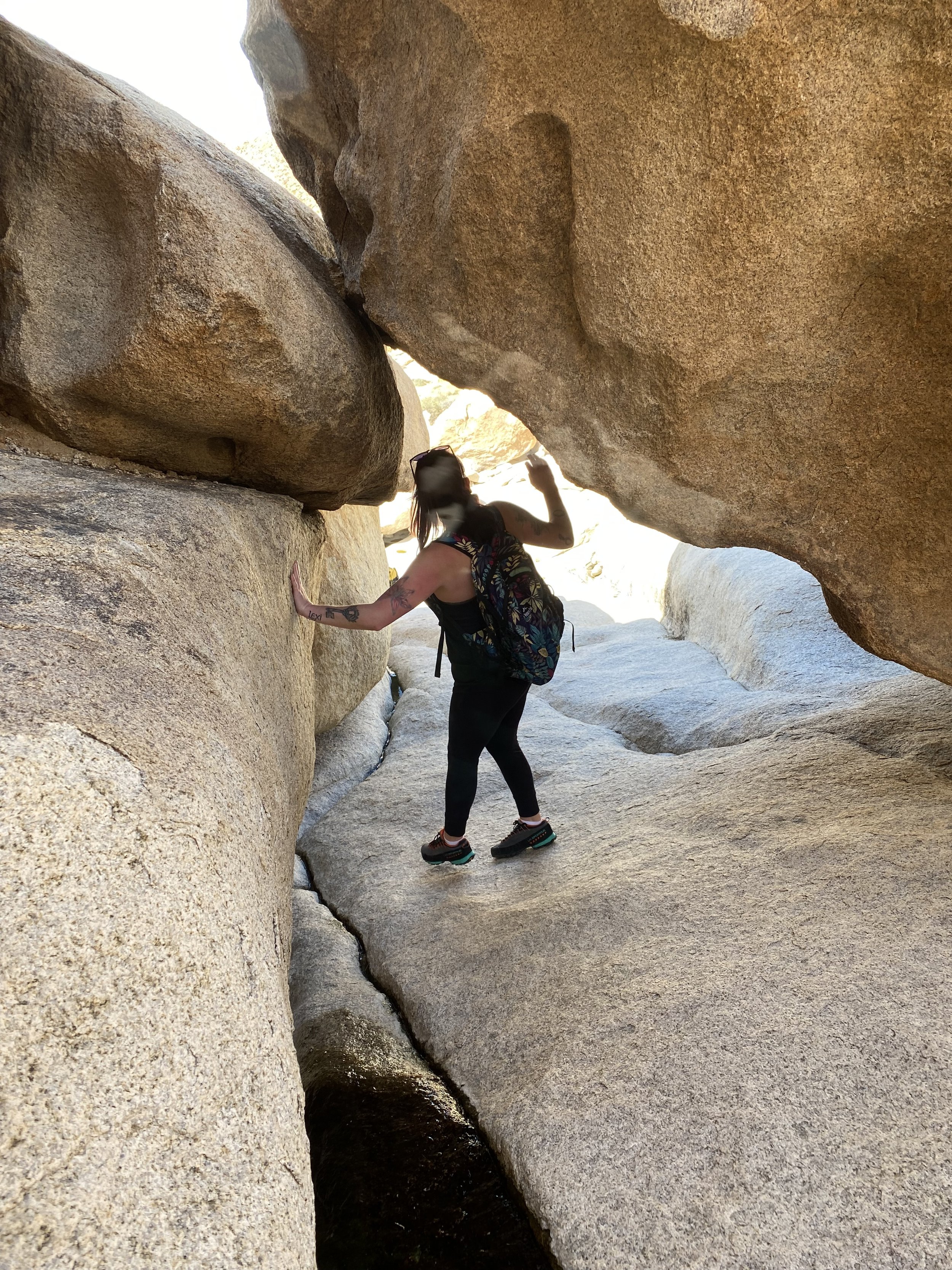 A woman with a backpack hiking through a narrow rocky canyon with large boulders overhead.