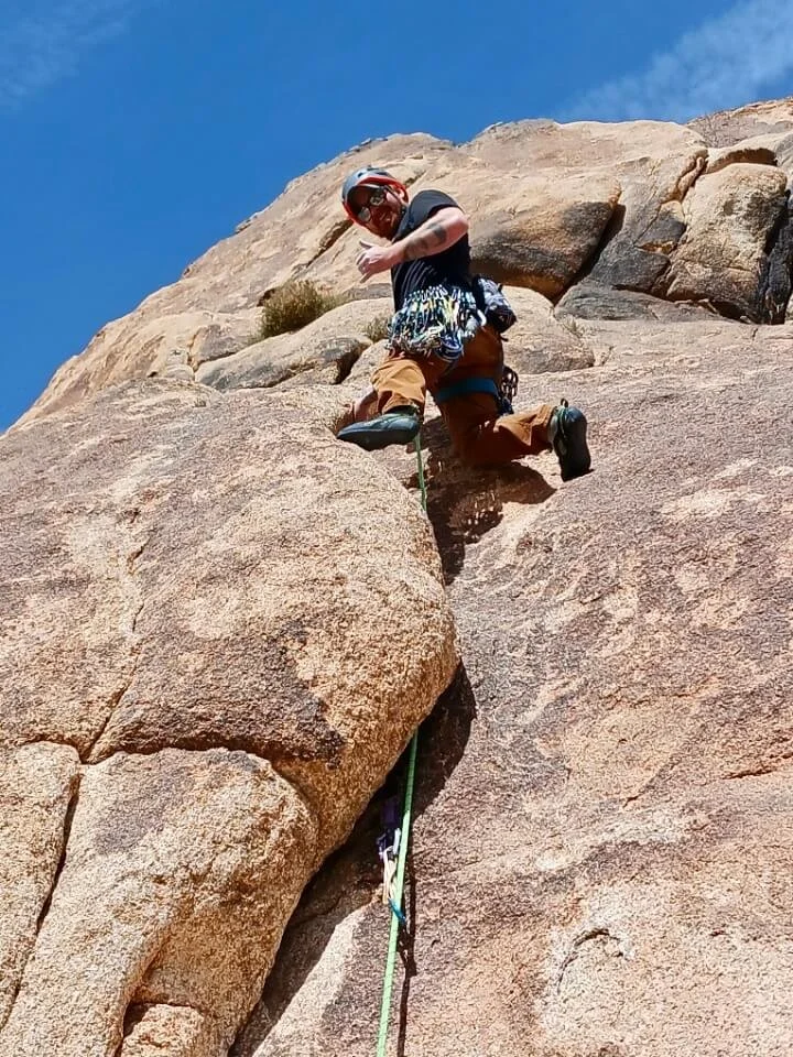 Climber leading a trad route on a steep granite face in Joshua Tree