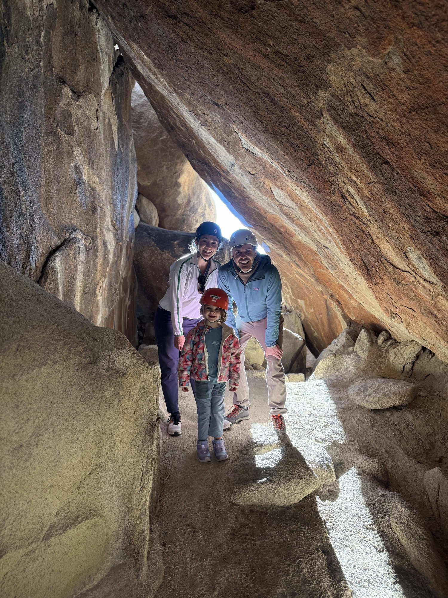 Family in helmets exploring a Joshua Tree cave corridor on a Summit Climbing Guides S1 tour