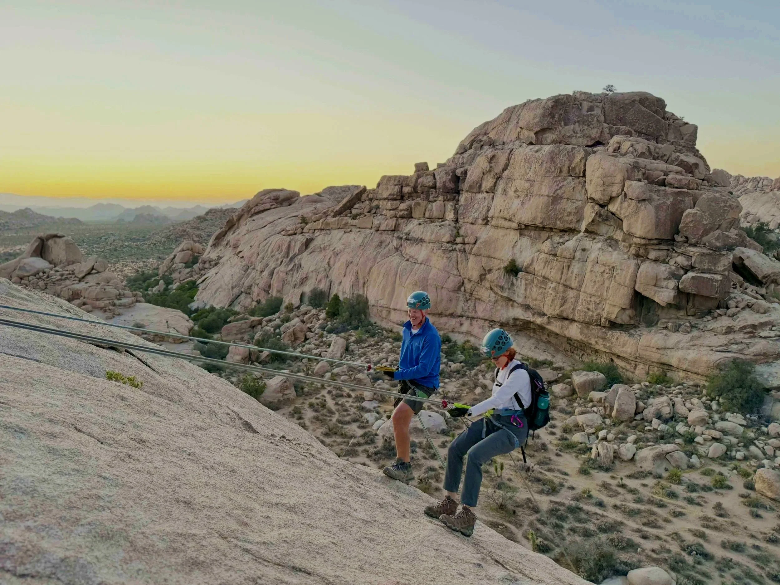 Rappelling at sunset in Joshua Tree National Park — climber descending against a glowing orange sky