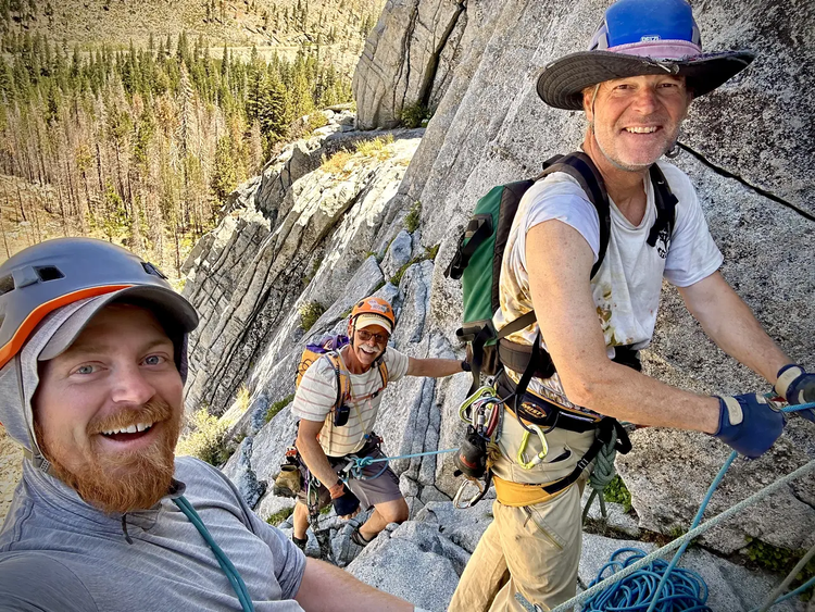 Three climbers with helmets and harnesses ascending a granite multi-pitch route