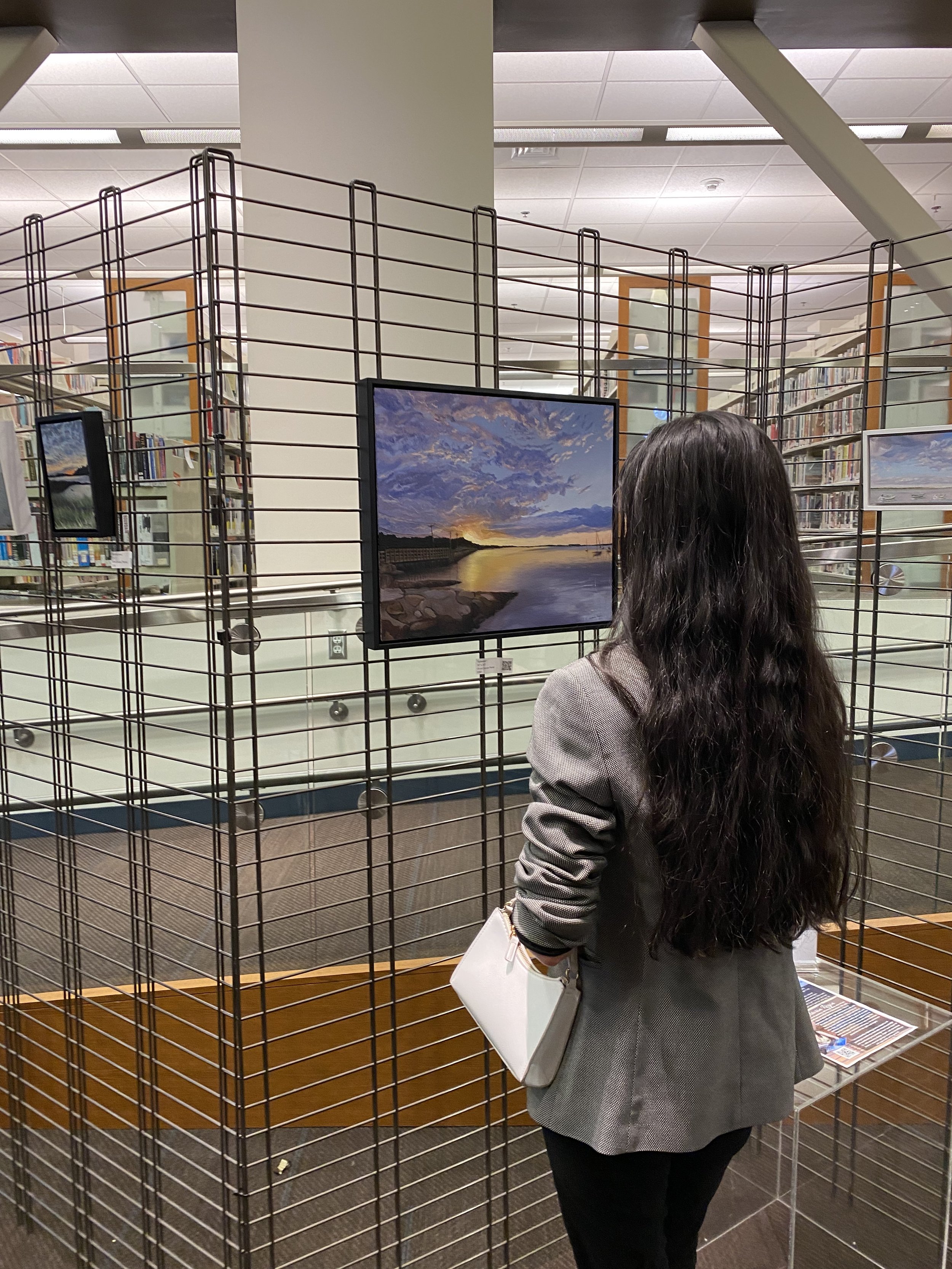Vitoria Regia looking at her favorite oil painting on display in her Art Exhibit in the art gallery room at Watertown Free Public Library, Massachusetts, April 2022. Vitoria Regia Paintings.