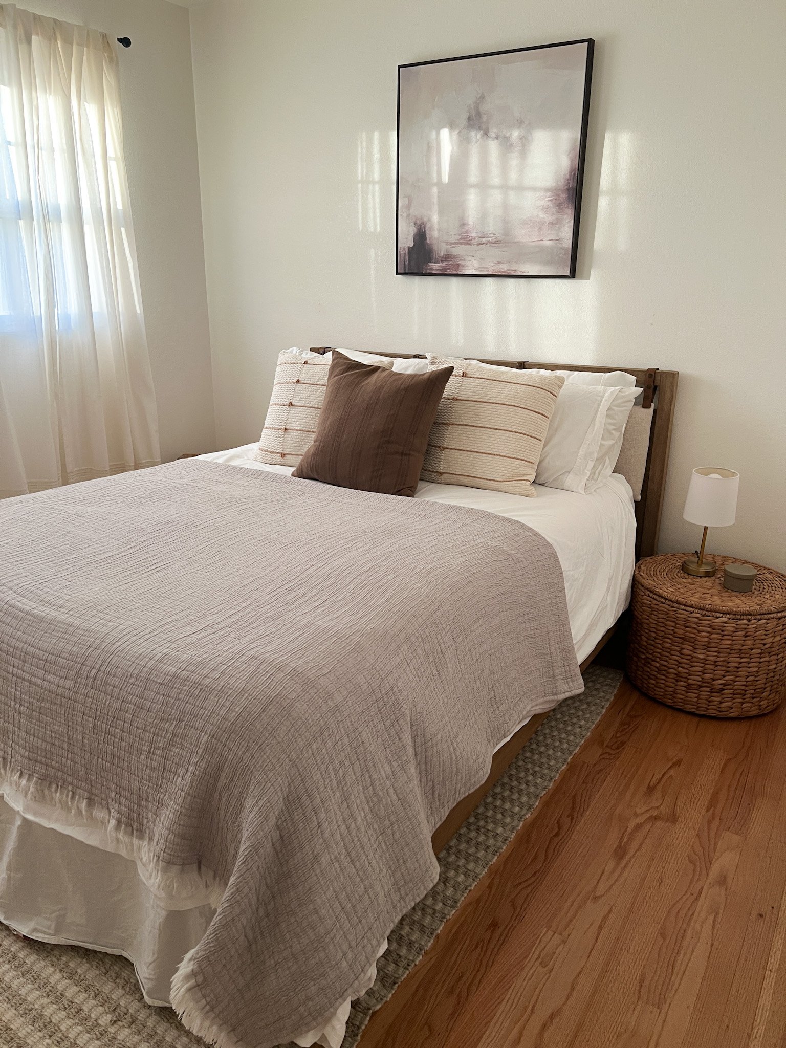 A peaceful bedroom with a rattan nightstand and abstract art 