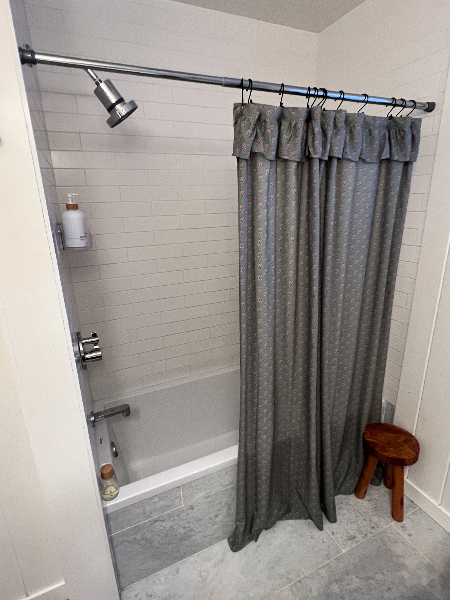 White subway tile shower and bath tub with shampoo and conditioner and floral shower curtain