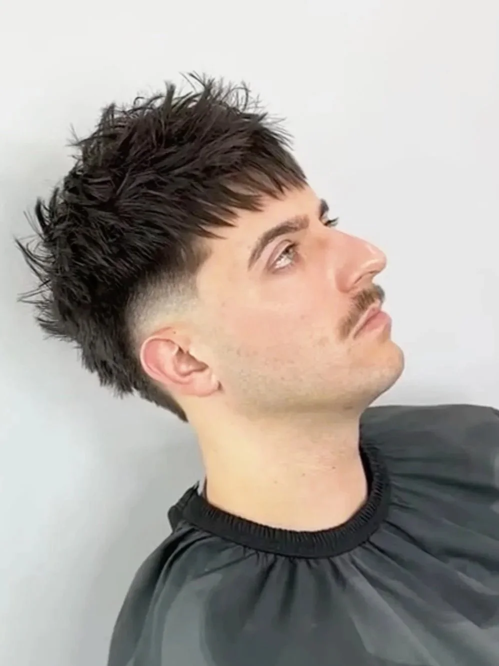 A young man with short, styled dark brown hair looking to the side against a plain white background.