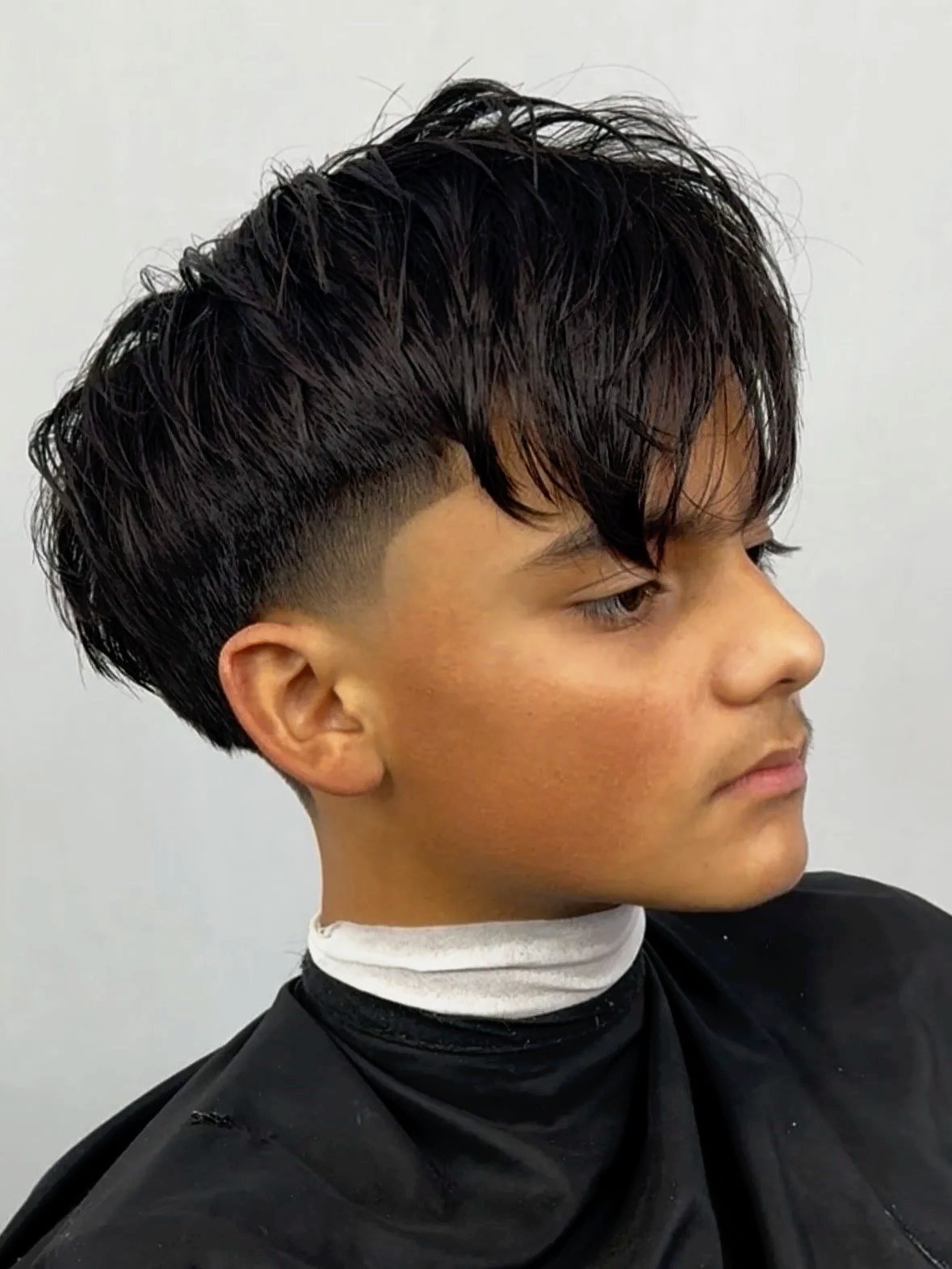Side view of a young man with a new haircut featuring a mid fade and full top.