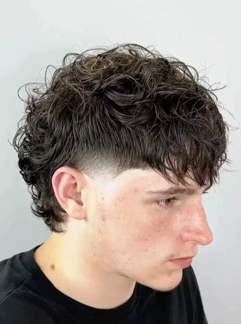Side profile of a young man with a fresh haircut, wearing a salon cape, against a plain light background.
