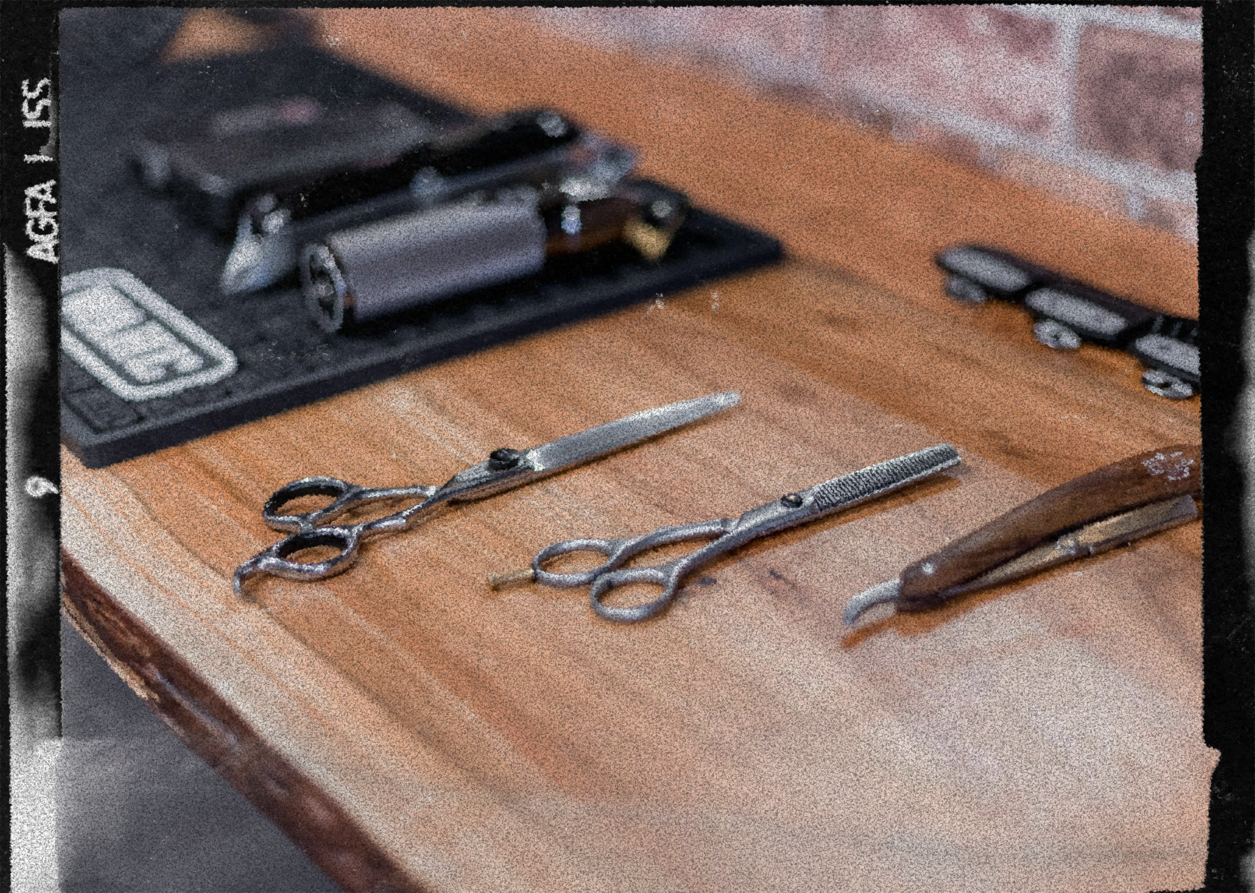 A wooden table with barber tools including two pairs of scissors, a straight razor, and a cartridge razor with a black case in the background.